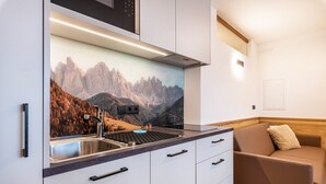 A kitchenette with a sink, stove, and cabinets, a sofa, and a mountain landscape mural. - Holiday Apartment "Planerhof Apartment Alpenrose" with Mountain View, Shared Terrace, and Wi-Fi (Funes)