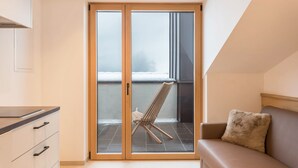 A room with a sliding glass door leading to a balcony with a chair, a sofa, and a cabinet with drawers.