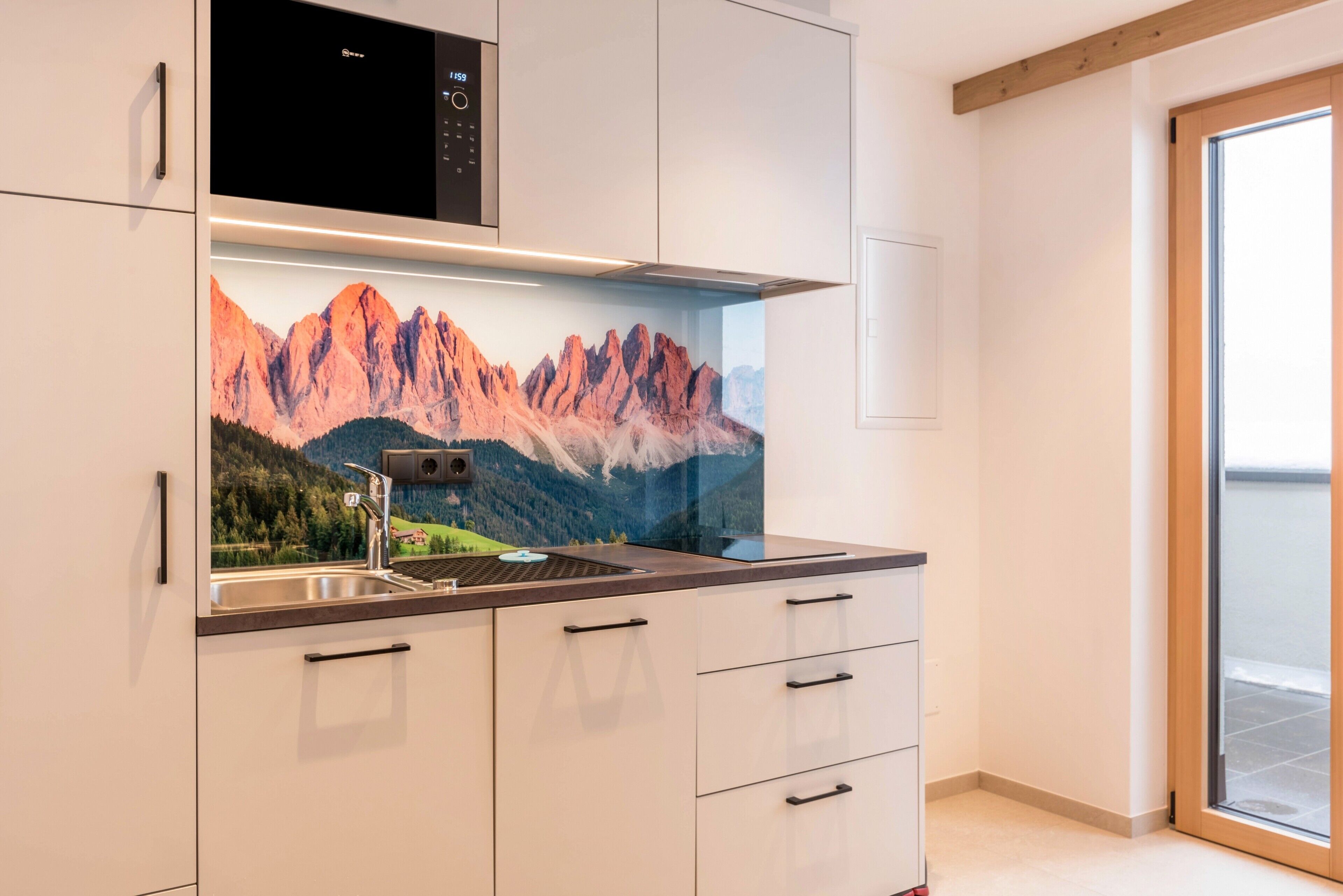 A modern kitchen with a mountain mural, stainless steel appliances, and a sliding glass door.