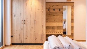 A room with a wooden wardrobe, a bed with neatly folded white linens, and a wooden bench.