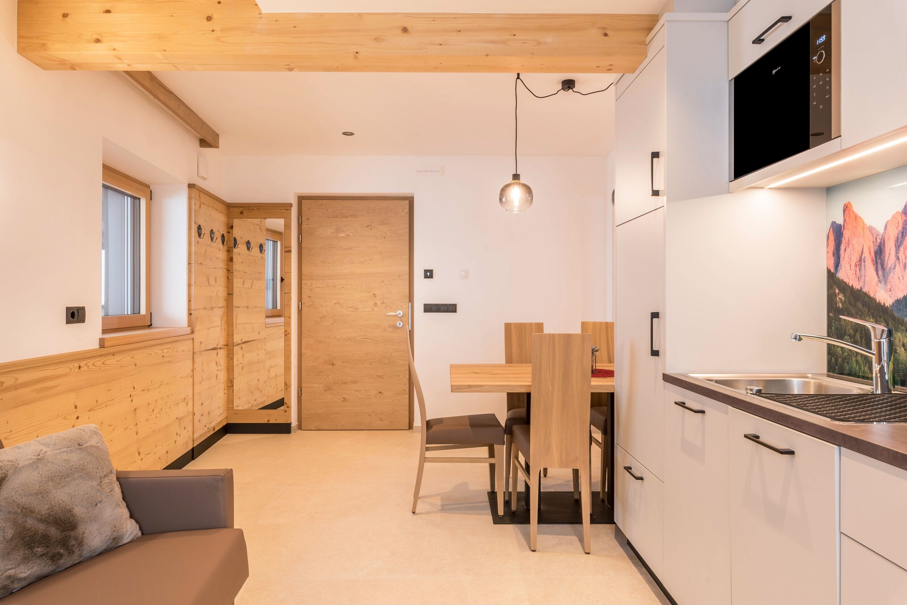 Een moderne keuken met houten kastjes, een ingebouwde magnetron en een eethoek met een houten tafel en stoelen.