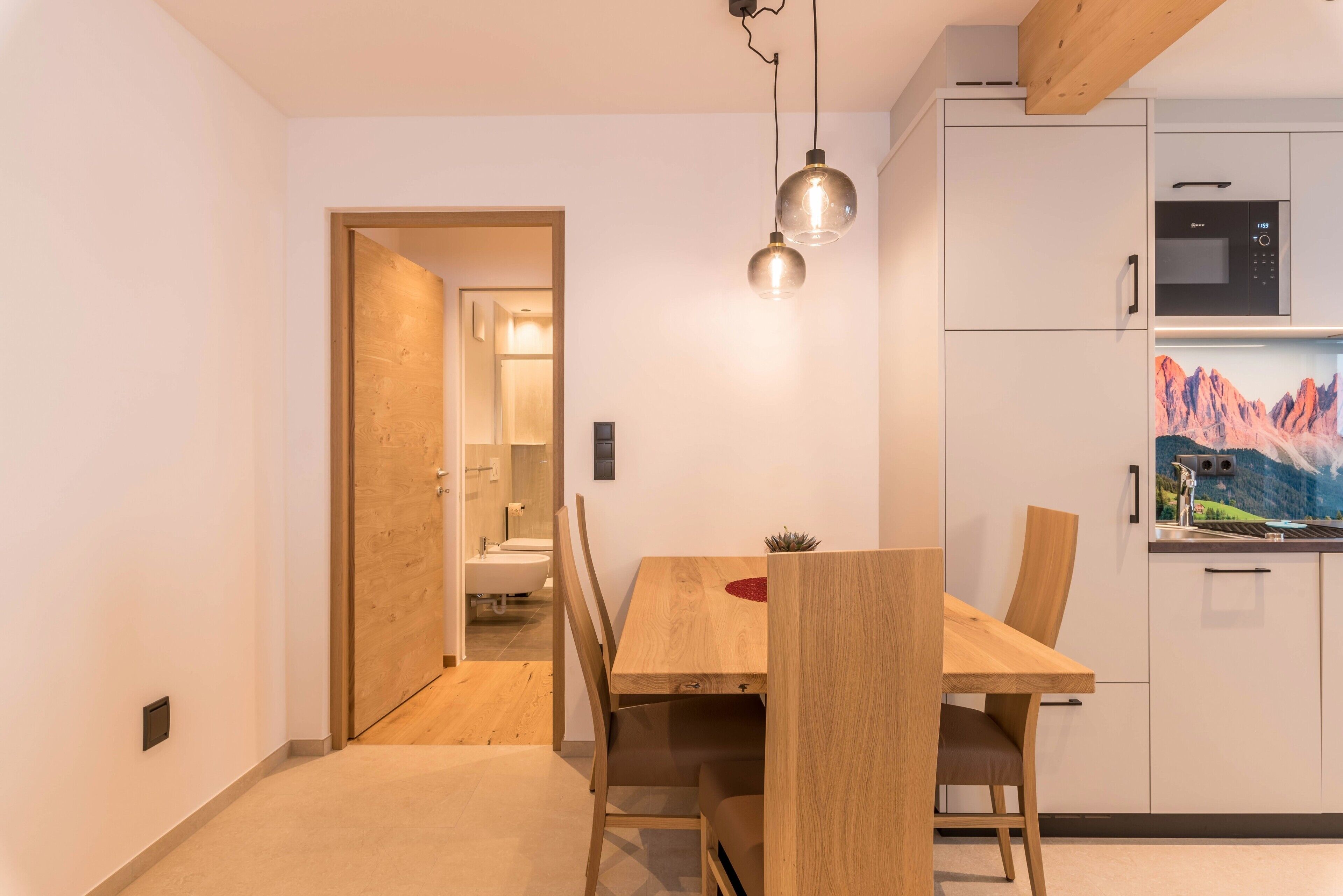Une cuisine moderne avec des meubles blancs, un four à micro-ondes et un coin repas comprenant une table et des chaises en bois.