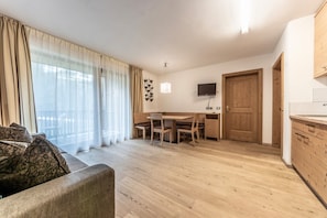 Una habitación con una mesa de comedor de madera, sillas, un sofá, un televisor y una cocina con armarios de madera.