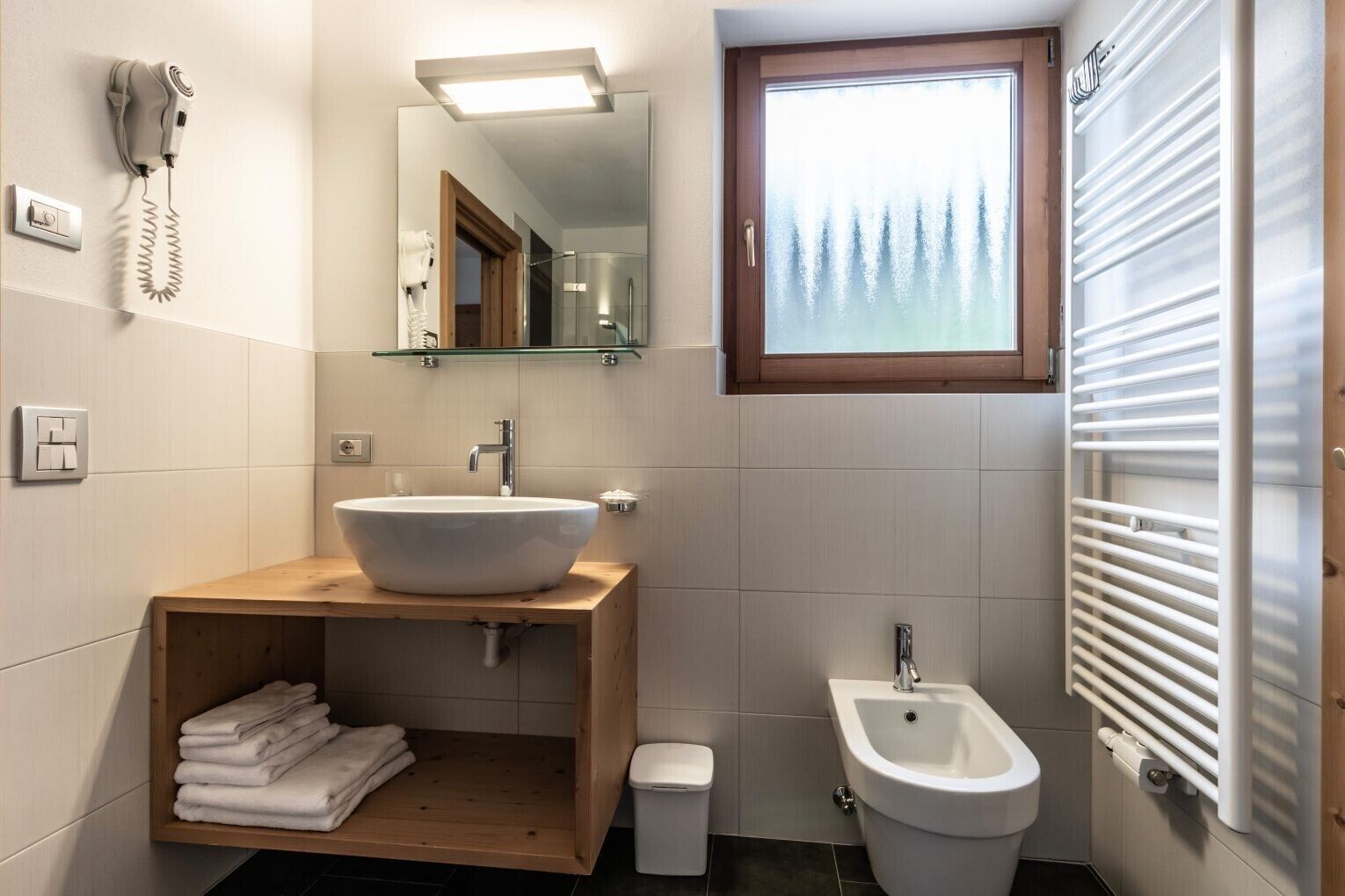 Un baño con un lavamanos grande, un bidé, un espejo, un secador de pelo y una ventana.