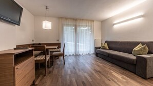 A modern living room with a wooden desk, a sofa, and a television mounted on the wall. - Apartment "Le Table C" with Mountain View, Garden & Wi-Fi (St. Vigil in Enneberg)