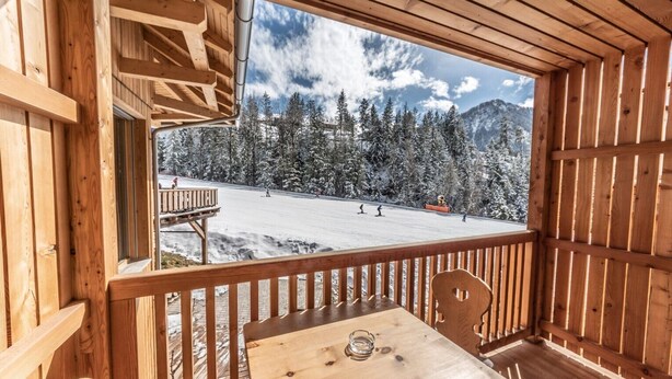 A wooden cabin with a balcony overlooking a snowy ski slope. - Apartment "Le Table E" with Mountain View, Garden & Wi-Fi (St. Vigil in Enneberg)