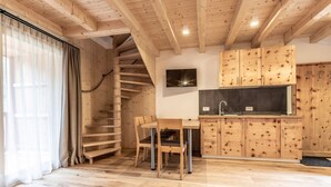 A wooden interior with a spiral staircase, a dining area, and a kitchen with wooden cabinets. - Apartment "Le Table E" with Mountain View, Garden & Wi-Fi (St. Vigil in Enneberg)