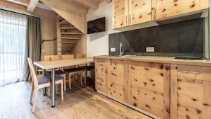 A modern kitchen with wooden cabinetry, a built-in stove, and a dining area with a table and chairs. - Apartment "Le Table E" with Mountain View, Garden & Wi-Fi (St. Vigil in Enneberg)
