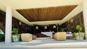 A covered outdoor seating area with woven furniture, a reception desk, and hanging lights. - TULUM loft in the Heart of Aldea Zama (Tulum)