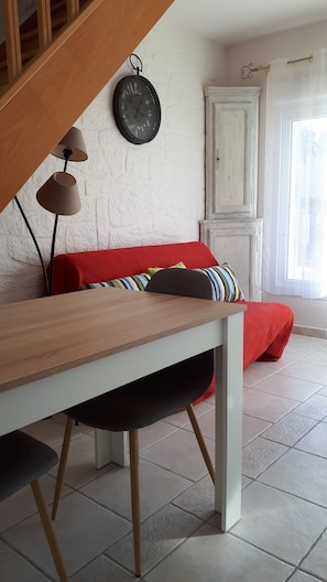 A room with a wooden table, a red sofa with striped cushions, a white cabinet, and a wall clock.