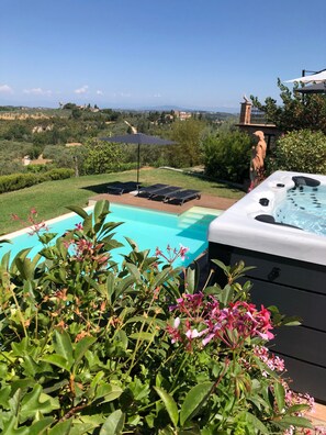 Un bain à remous avec une piscine et des chaises longues, le tout entouré de verdure et offrant une vue panoramique.
