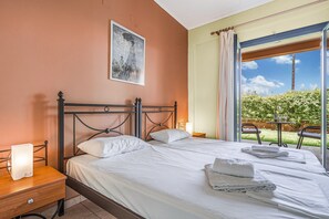 A hotel room with a bed, a bedside table, a lamp, a painting on the wall, and a view of the outdoors.