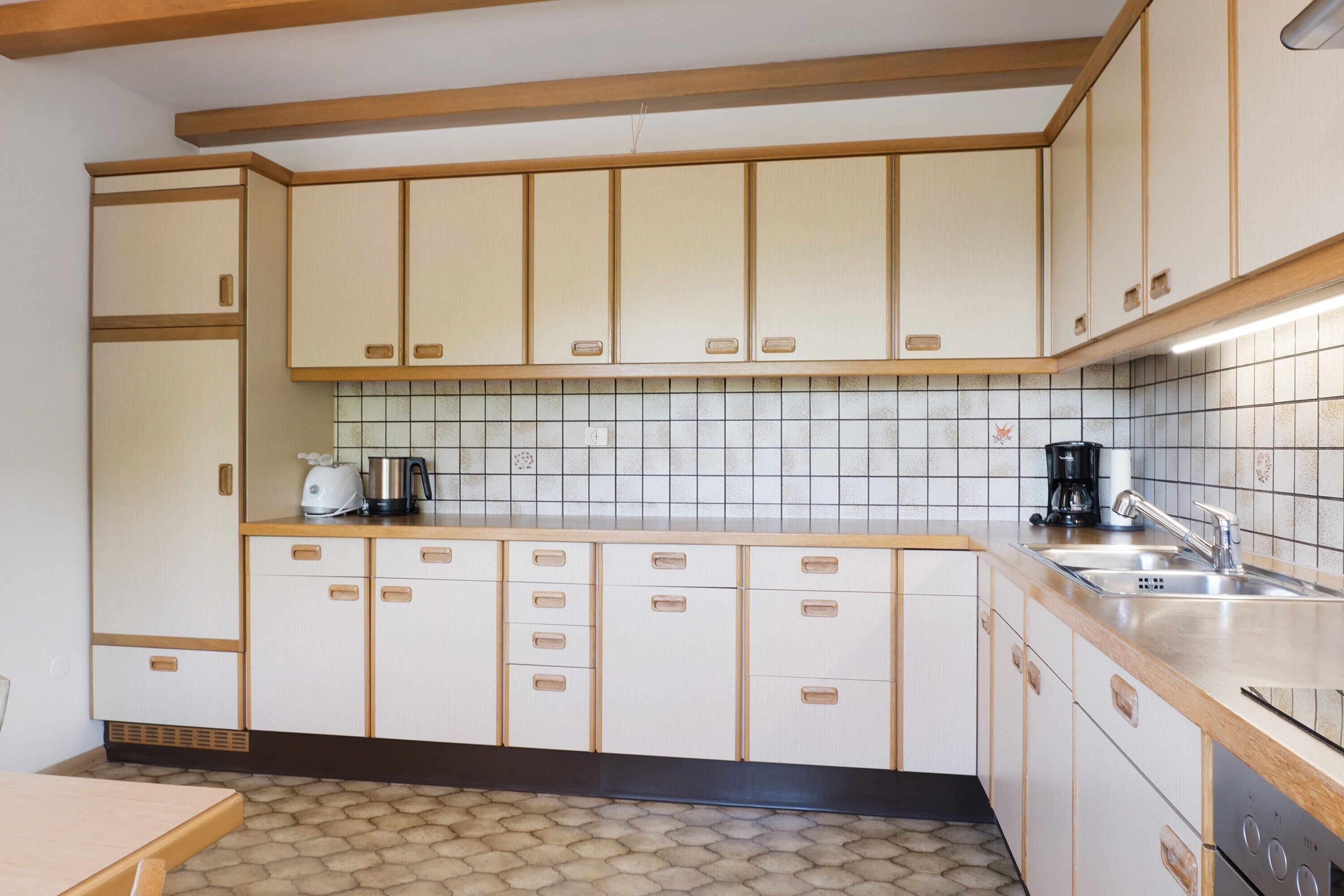 Una cocina con armarios de madera, salpicadero de azulejos y encimera con cafetera y hervidor.