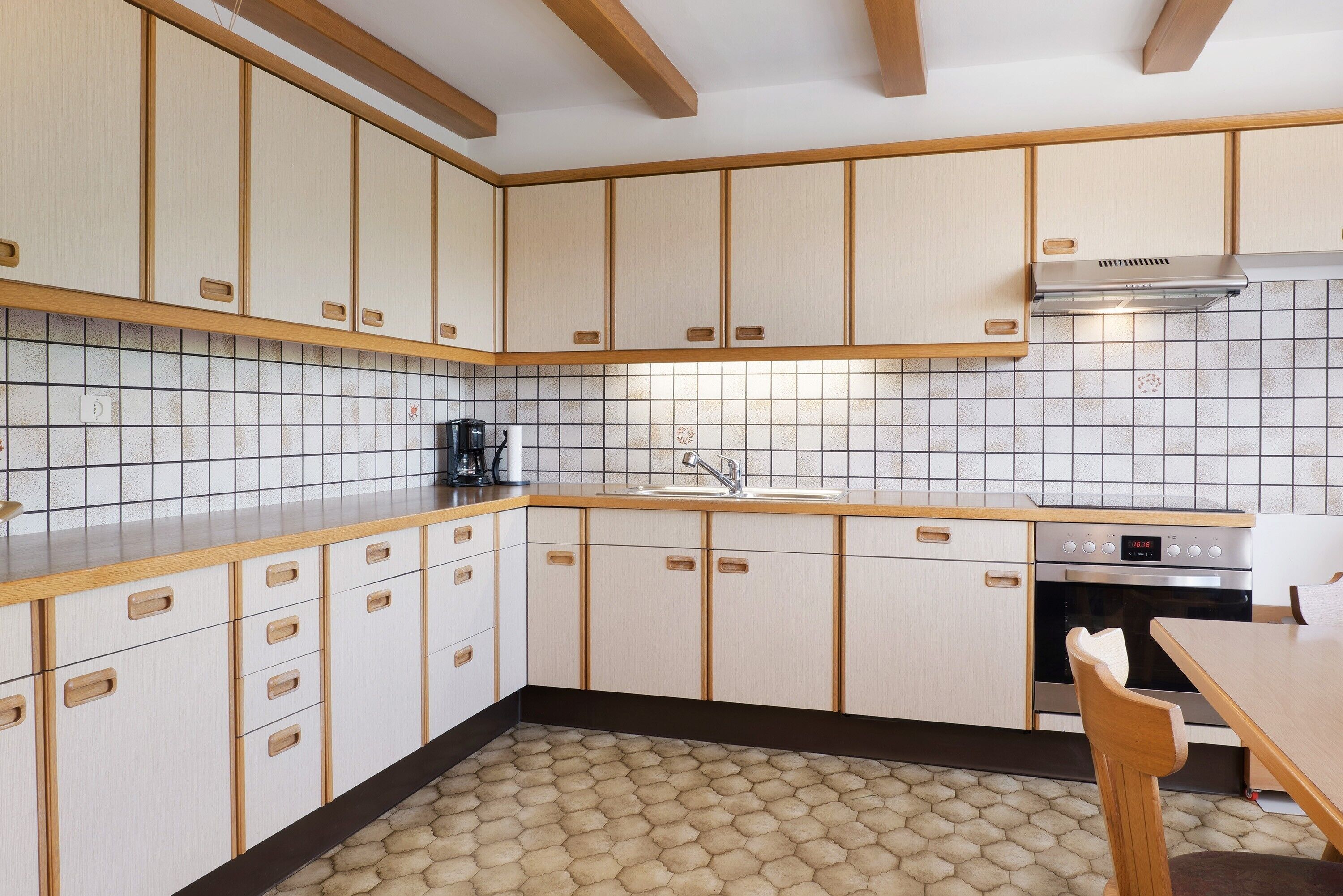 A kitchen with wooden cabinets, a tiled backsplash, a stove, and a dining area with a chair.