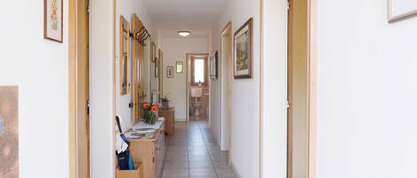 Un couloir avec des portes en bois, des œuvres d’art encadrées, un sol carrelé et un coin cuisine équipé d’un évier et d’un plan de travail.