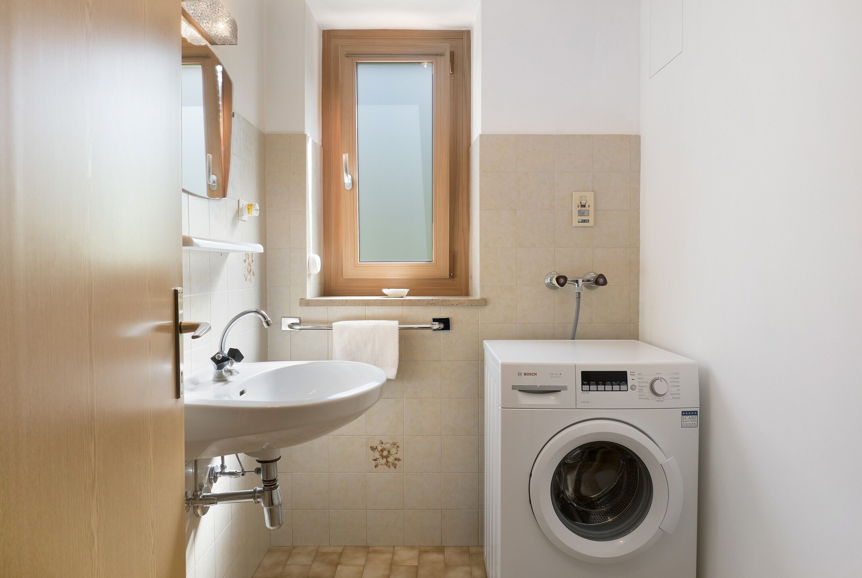 Un bagno piccolo ma funzionale, con lavandino, specchio, finestra e lavatrice.