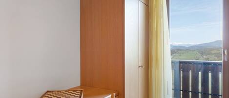Ein Zimmer mit einem Holztisch, einem Schachbrett und Blick auf einen Balkon mit Geländer.