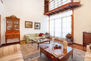Un salón espacioso con techo alto, un sofá verde, una mesa de centro de madera y un mueble grande.