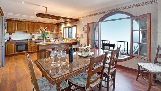 A spacious kitchen with wooden cabinets, a dining area with a large table and chairs, and a view through a large window. - Vacation Home "La Victoria' with Sea View, Private Terrace & Wi-Fi (La Victoria)