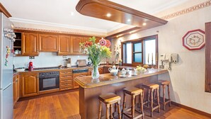 A kitchen with wooden cabinets, a central island with stools, a built-in oven, and a decorative clock on the wall. - Vacation Home "La Victoria' with Sea View, Private Terrace & Wi-Fi (La Victoria)