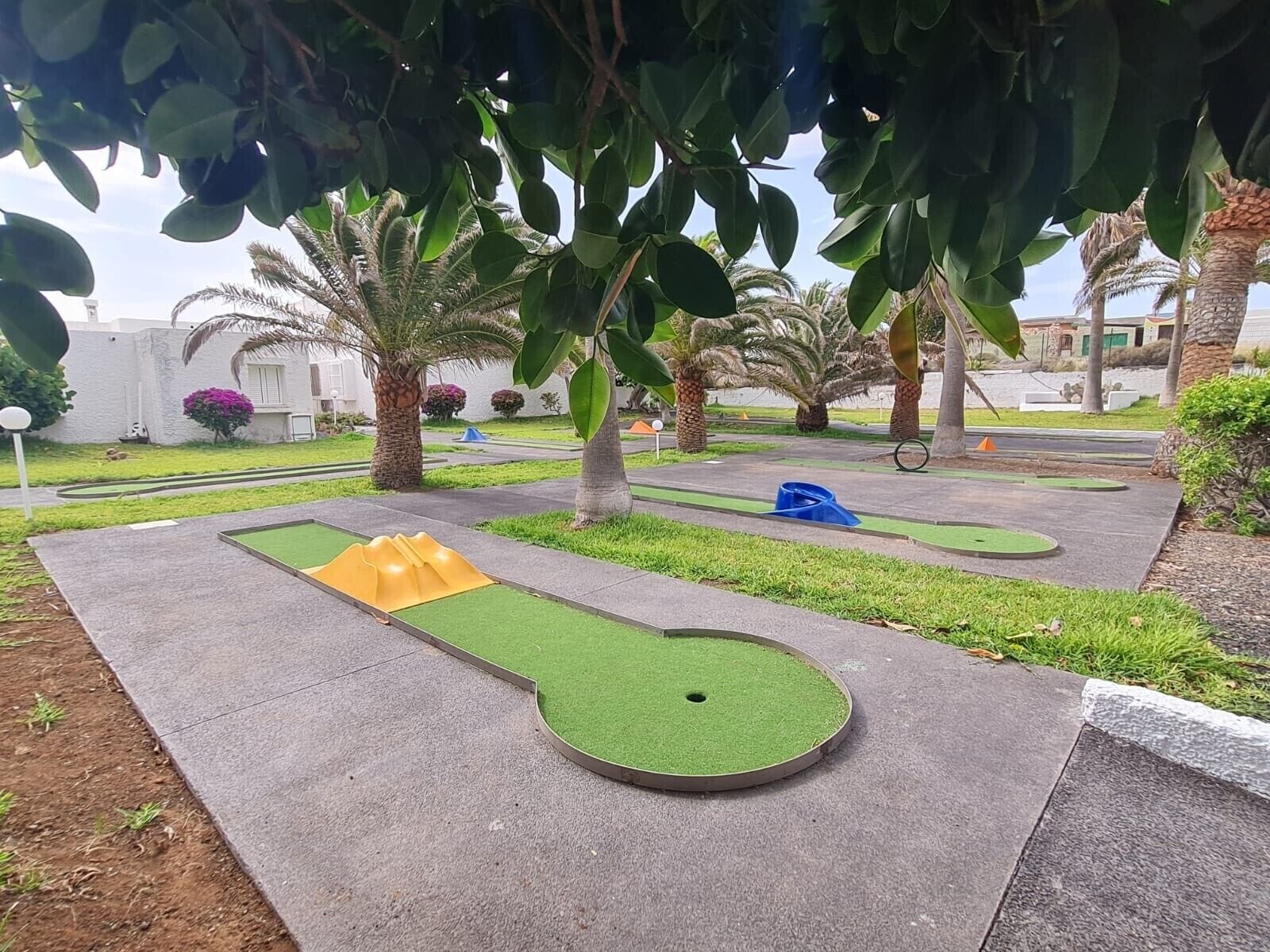 Un campo de mini golf con un área de juego verde, una rampa amarilla y un hoyo azul.