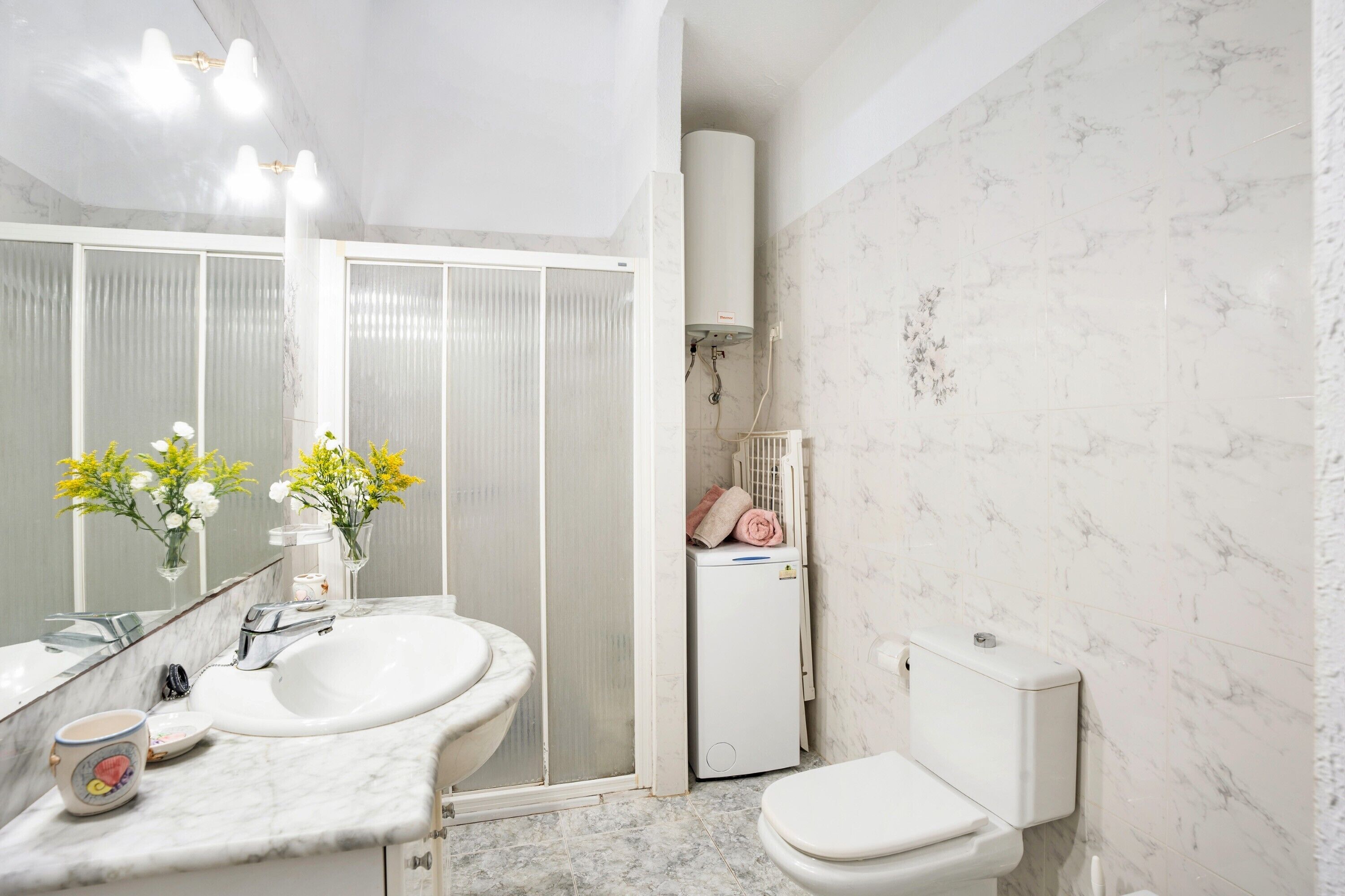 A bathroom with a white sink, mirror, toilet, and shower enclosure.