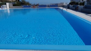 A clear blue swimming pool with a metal ladder, surrounded by modern buildings and a clear sky. - Holiday Apartment "Poris" with Heated Pool, Private Terrace & Wi-Fi (Arico)