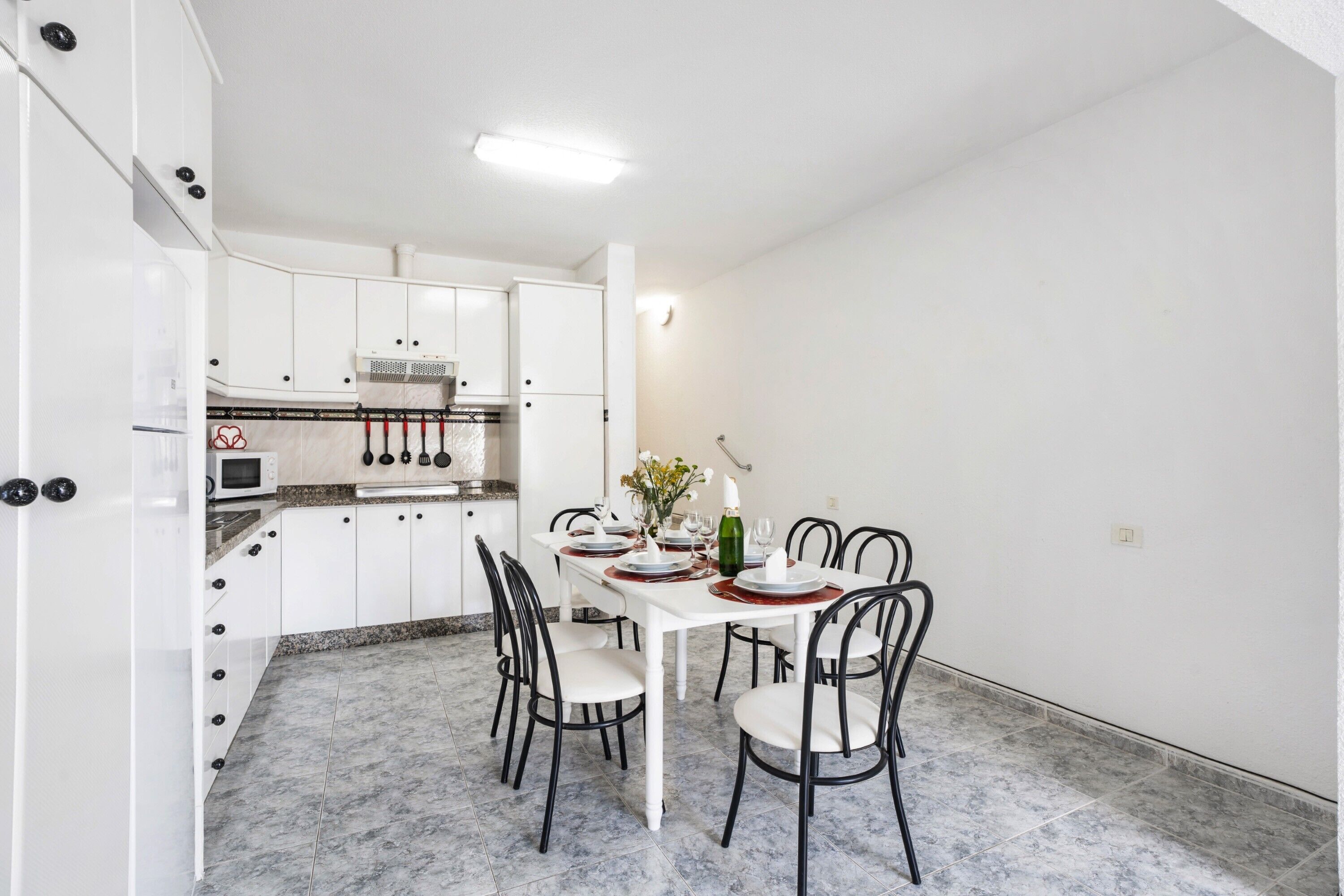 A compact kitchen with white cabinets, a dining table set for four, and a microwave.