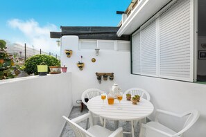 A white outdoor patio with a round table and chairs, potted plants, and decorative wall items.