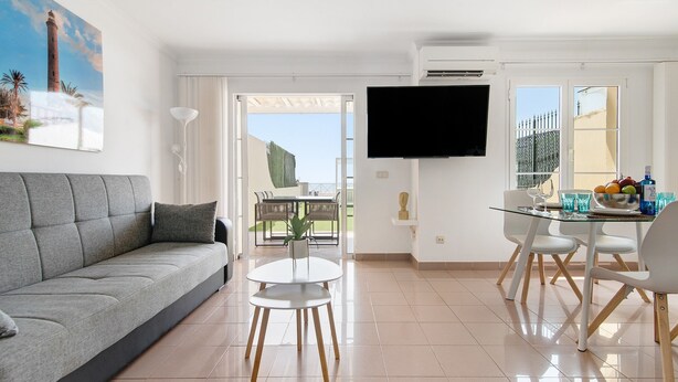 Un salon moderne comprenant un canapé, une table à manger avec des chaises, un téléviseur à écran plat et un balcon avec vue.