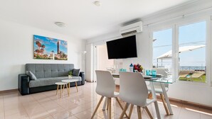 Un salon moderne comprenant un canapé, une table à manger, des chaises, un téléviseur à écran plat et de grandes fenêtres offrant une vue dégagée.