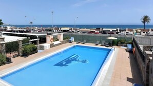 Une piscine sur le toit offrant une vue sur l’océan, entourée d’immeubles et d’un parking.