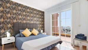 Une chambre avec un grand lit, une table de chevet, un banc et une vue sur l’extérieur.