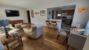 Ein modernes Wohnzimmer mit Sofa, Couchtisch und Fernseher. Dazu eine Küchenzeile mit Esstisch und Stühlen.