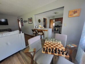 Un salon avec un jeu d’échecs, un canapé, un téléviseur et une cuisine en arrière-plan.