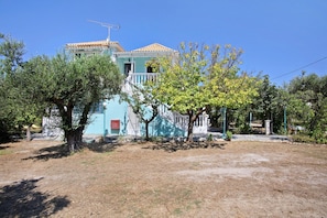A two-story building with a balcony, surrounded by trees and a clear sky.