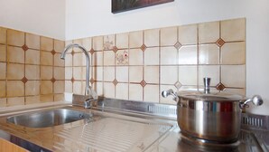 A kitchen with a stainless steel sink, a pot on the stove, and decorative tiles on the backsplash.