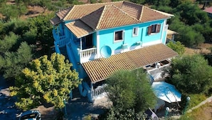 A two-story house with a tiled roof, surrounded by greenery and a clear sky.