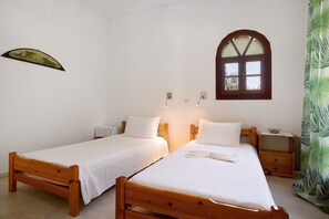 Une pièce avec deux lits en bois, une petite fenêtre et un luminaire fixé au mur.