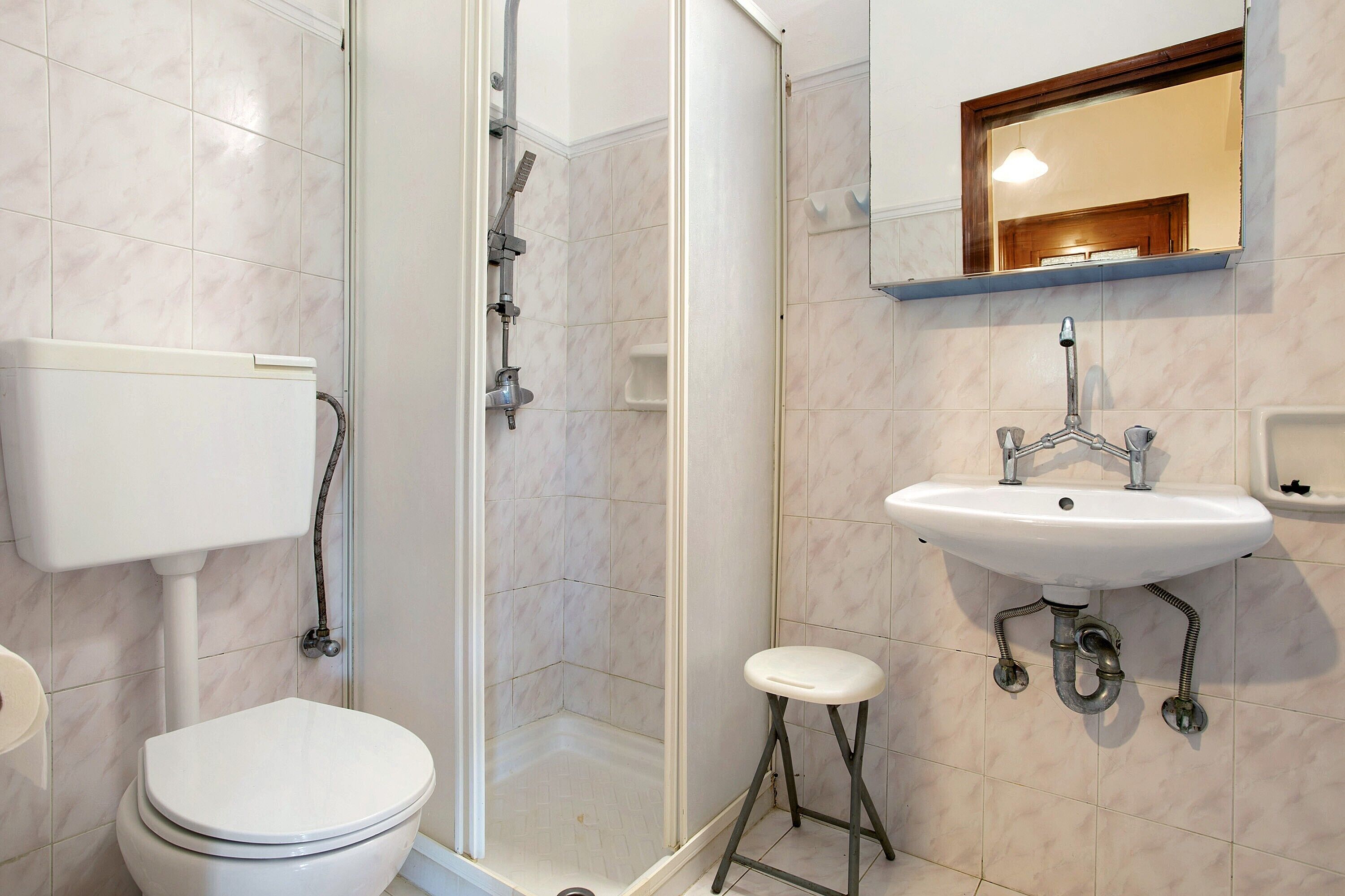 Un baño con inodoro, ducha, lavamanos y espejo.
