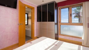 Un dormitorio con cama, armario, televisor y ventana con vistas.