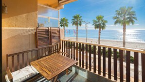 Un balcón con una mesa y sillas de madera, con vistas a una playa con palmeras y el océano.