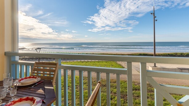 A balcony with a view of the ocean, a table with plates and glasses, and a railing. - Apartment "Didier" with Sea View, Terrace & Wi-Fi (Mimizan)