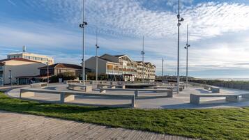 A coastal promenade with a circular seating area, street lamps, and a row of buildings with balconies.