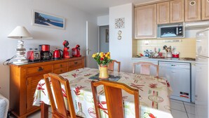 A compact kitchen with wooden cabinets, a microwave, a dishwasher, and a dining table with chairs. - Apartment "Didier" with Sea View, Terrace & Wi-Fi (Mimizan)