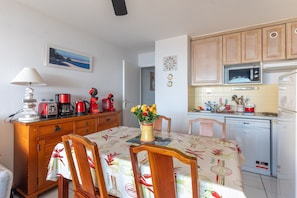 A compact kitchen with wooden cabinets, a microwave, a dishwasher, and a dining table with chairs. - Apartment "Didier" with Sea View, Terrace & Wi-Fi (Mimizan)