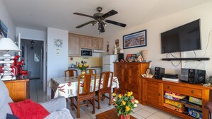 A living room with a sofa, a coffee table with a vase of flowers, a dining area with a table and chairs, a kitchen with cabinets and appliances, and a ceiling fan. - Apartment "Didier" with Sea View, Terrace & Wi-Fi (Mimizan)