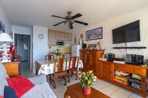 A living room with a sofa, a coffee table with a vase of flowers, a dining area with a table and chairs, a kitchen with cabinets and appliances, and a ceiling fan. - Apartment "Didier" with Sea View, Terrace & Wi-Fi (Mimizan)