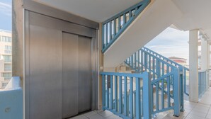 A modern building with a metal elevator, blue railings, and a tiled floor. - Apartment "Didier" with Sea View, Terrace & Wi-Fi (Mimizan)