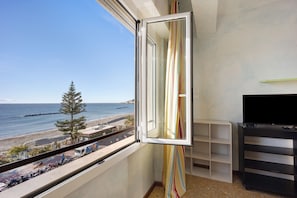 Varanda com vista para a praia, um suporte para televisão e uma cortina listrada.
